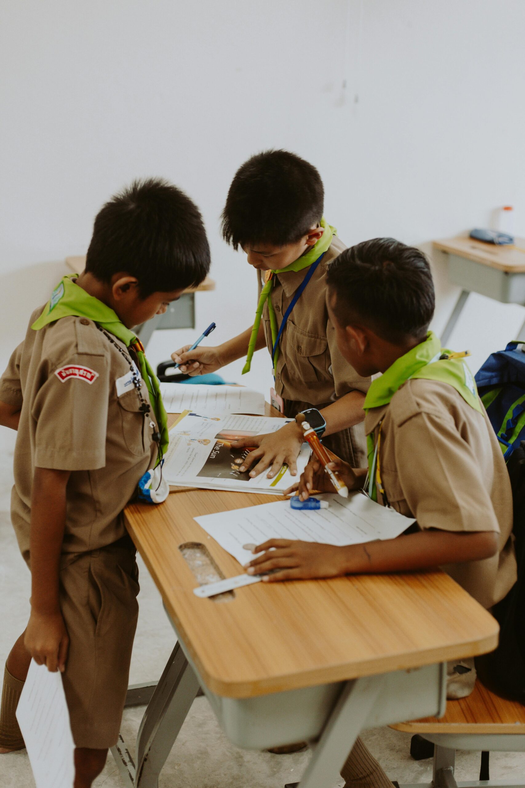 Children in school uniforms working together at a desk in a classroom.